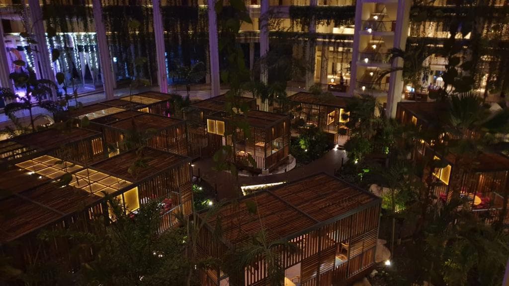 Aerial view of Lemon Fish restaurant at night — timber pavilion pods with amber lighting inside Paradisus hotel atrium