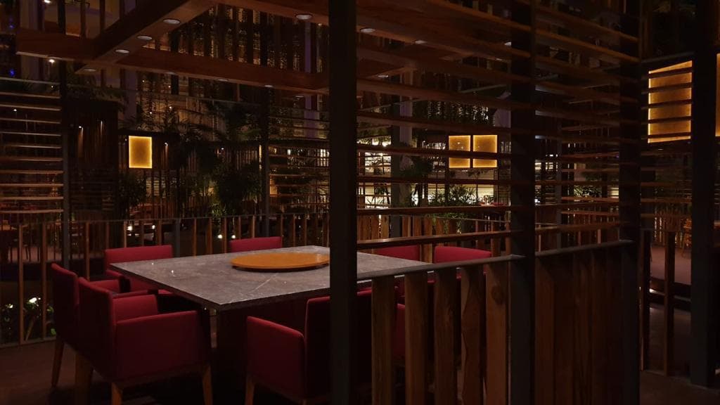 Interior de un comedor de noche — mesa de mármol gris, sillas tapizadas en rojo, paneles de tablillas de madera