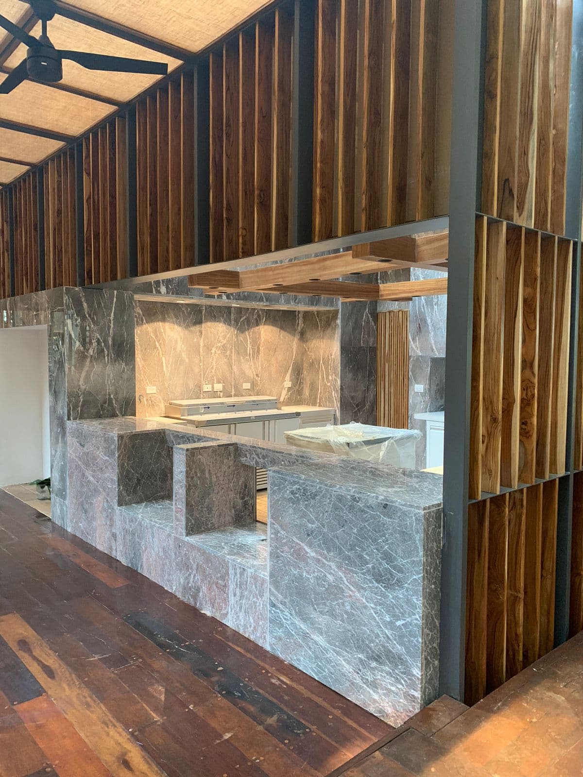 Mostrador de mármol enmarcado por muros de tablillas de madera a toda altura — área de barra