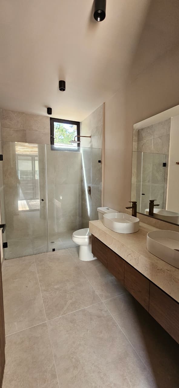 Casa Juuba — baño secundario con mampara de vidrio y vanidad de madera